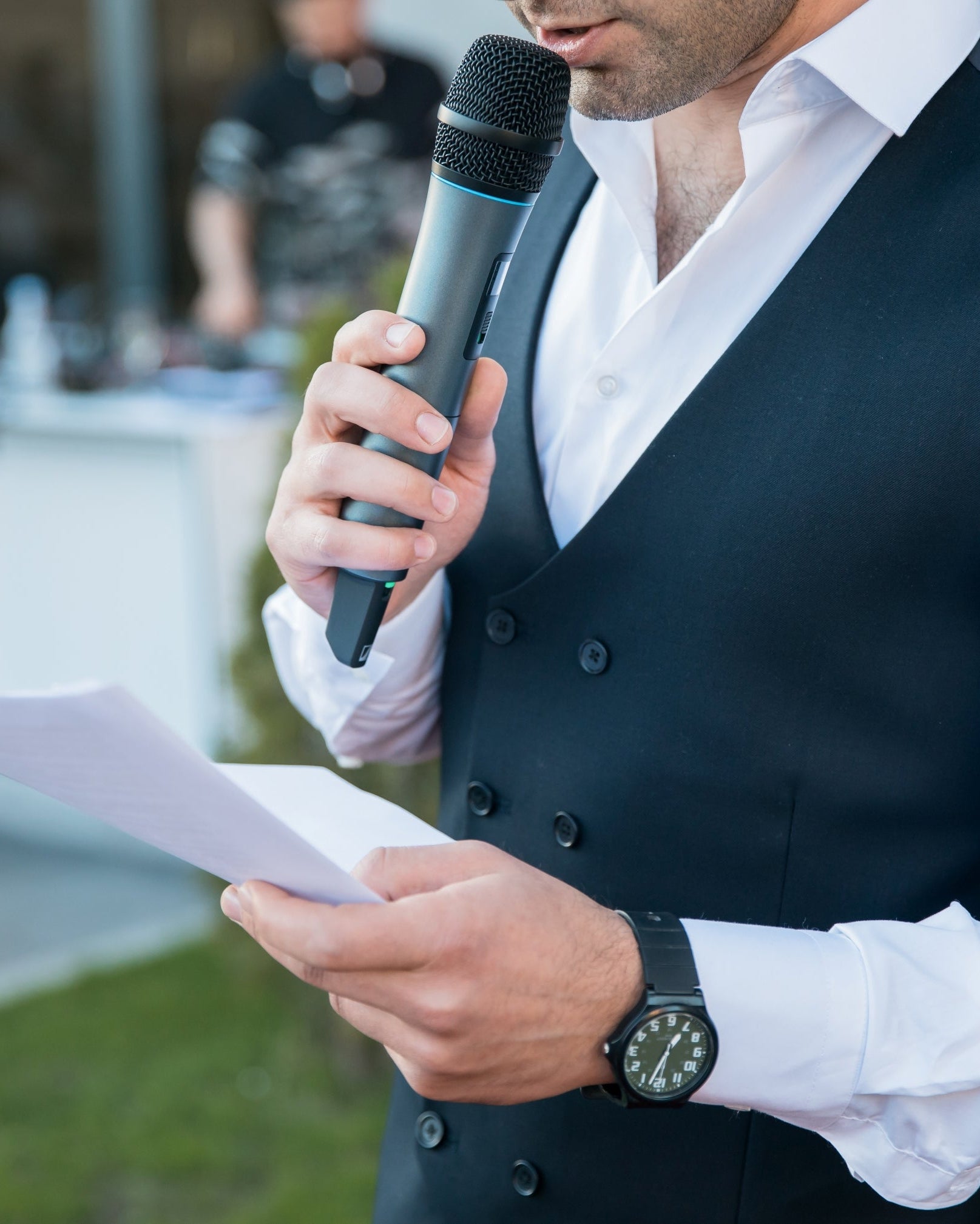 Man in formal attire holding a microphone and papers, likely giving a speech or presentation.