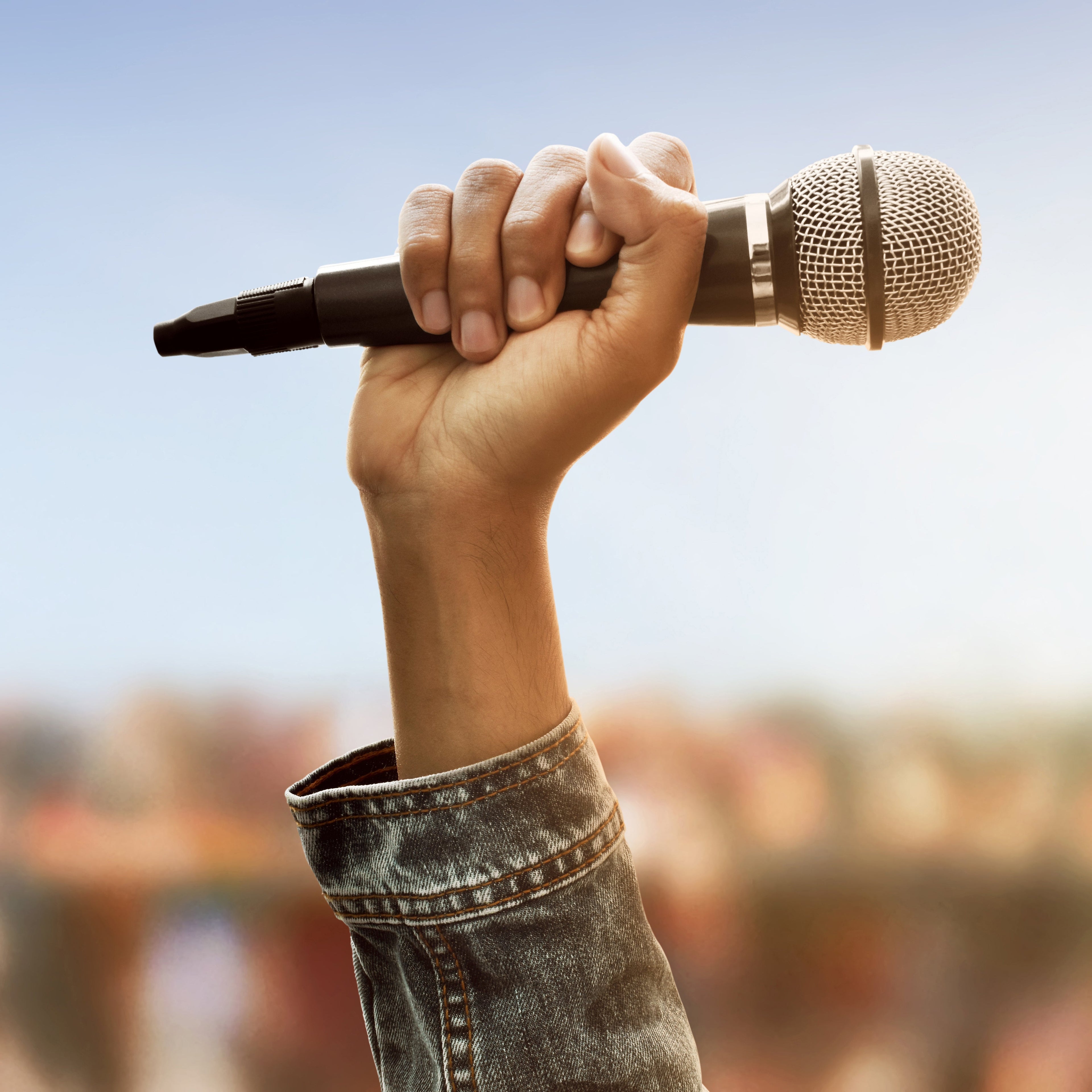 Hand holding a microphone against a blurred outdoor background