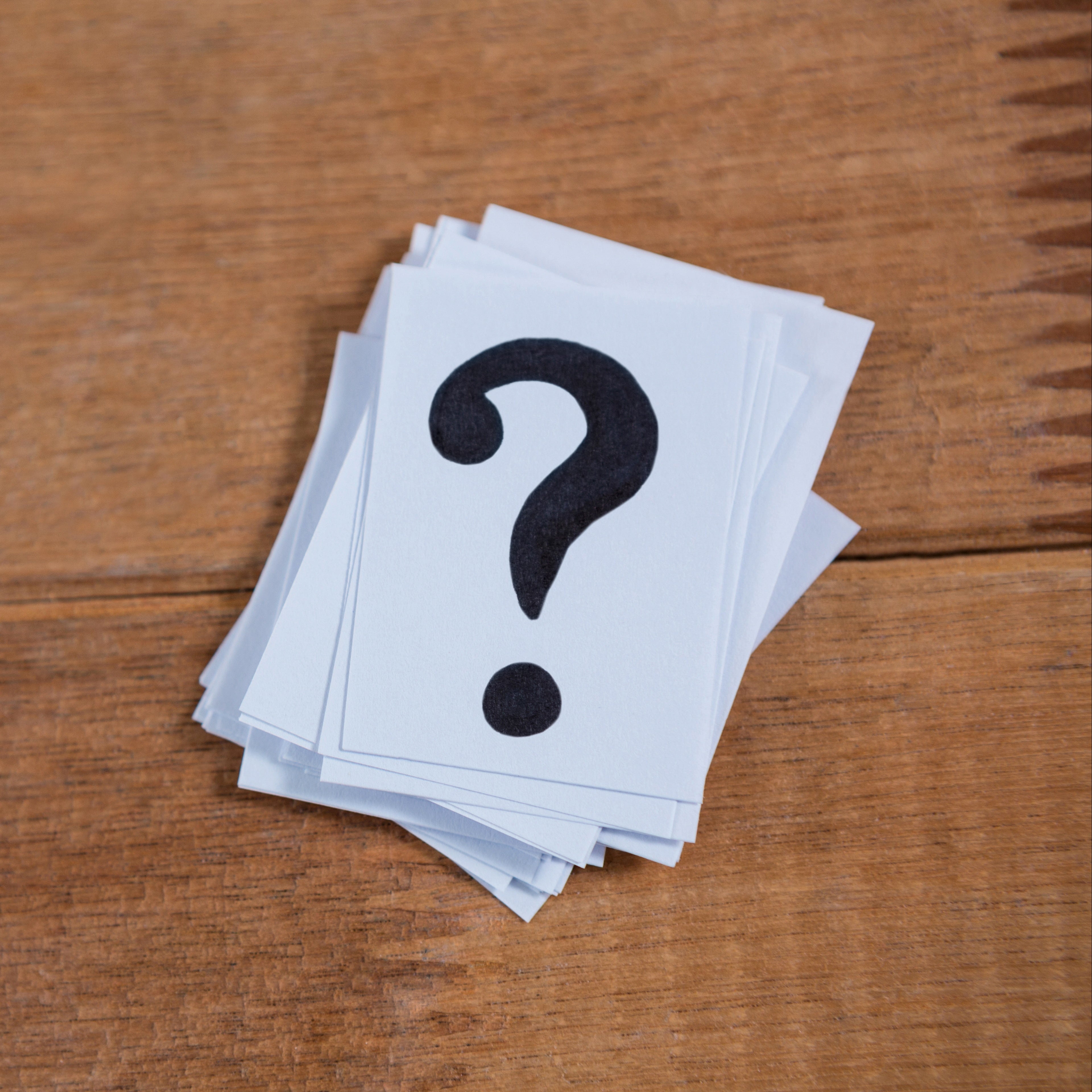 Stack of cards with question marks on a wooden surface